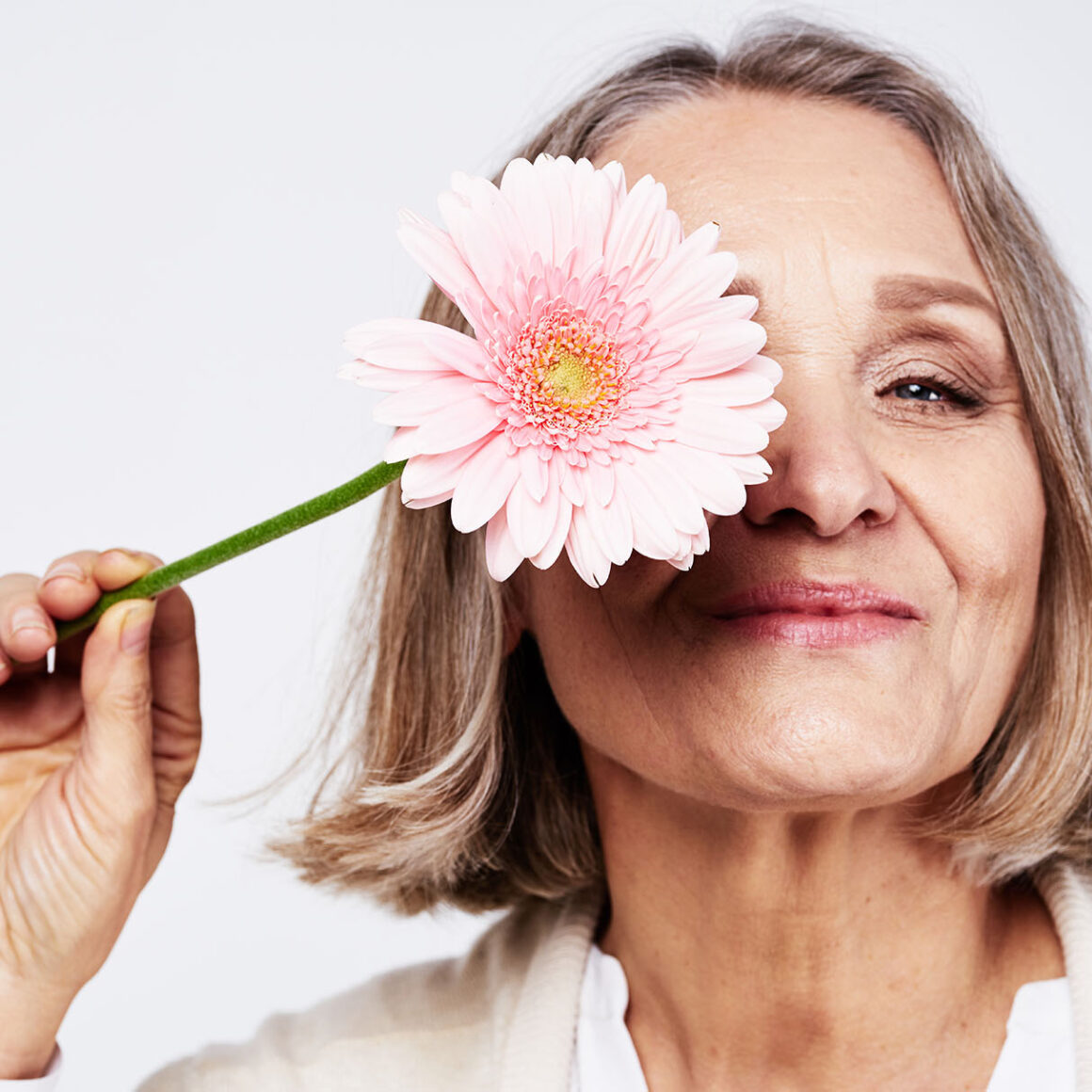 Eine Frau hält sich die Blüte einer Blume vor ihr eines Auge.