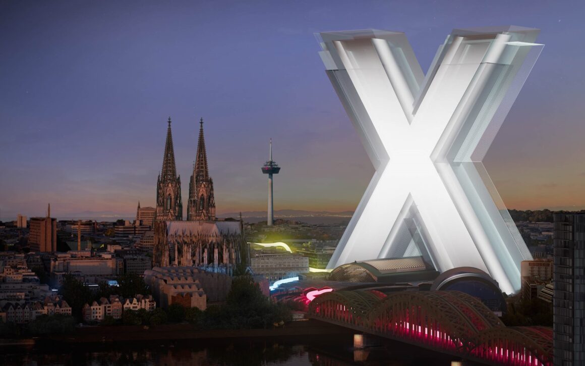 Ein großes X das für die Veranstaltung Digital X steht, überragt die Skyline von Köln bei Nacht