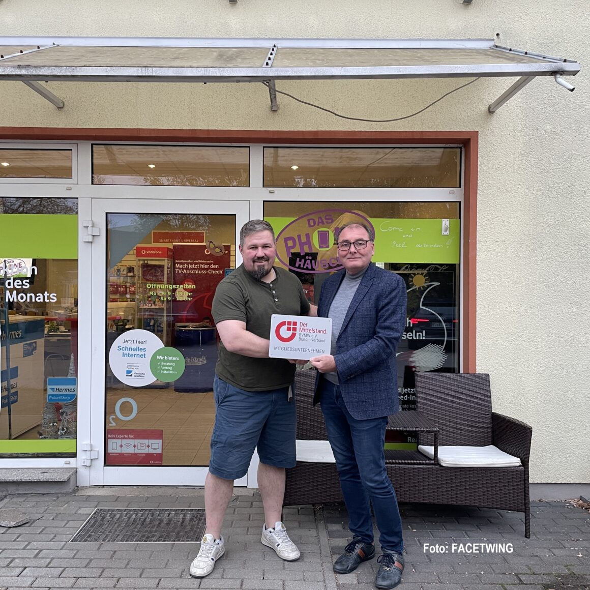 zwei Männer stehen vor einem Telefonladen und halten ein Schild in der Hand