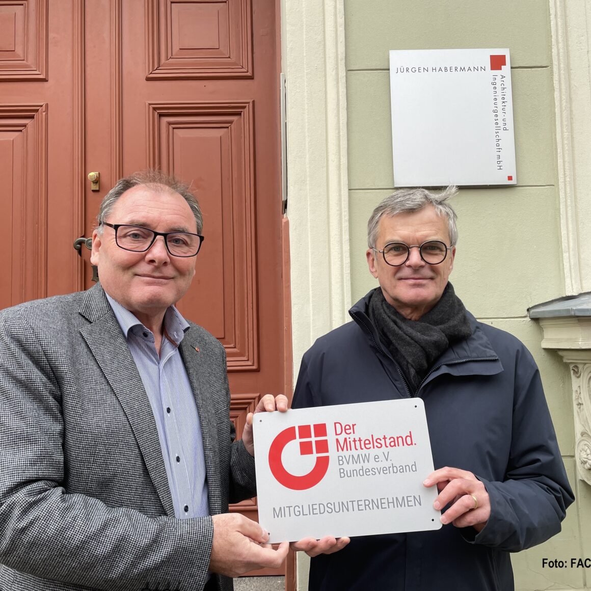 Zwei Männer stehen vor einem Gebäude und halten ein Schild in die Höhe