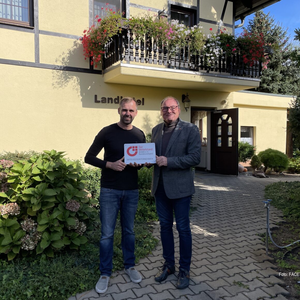 zwei Männer stehen vor dem Eingang eines Hotels und halten ein Schild in die Höhe