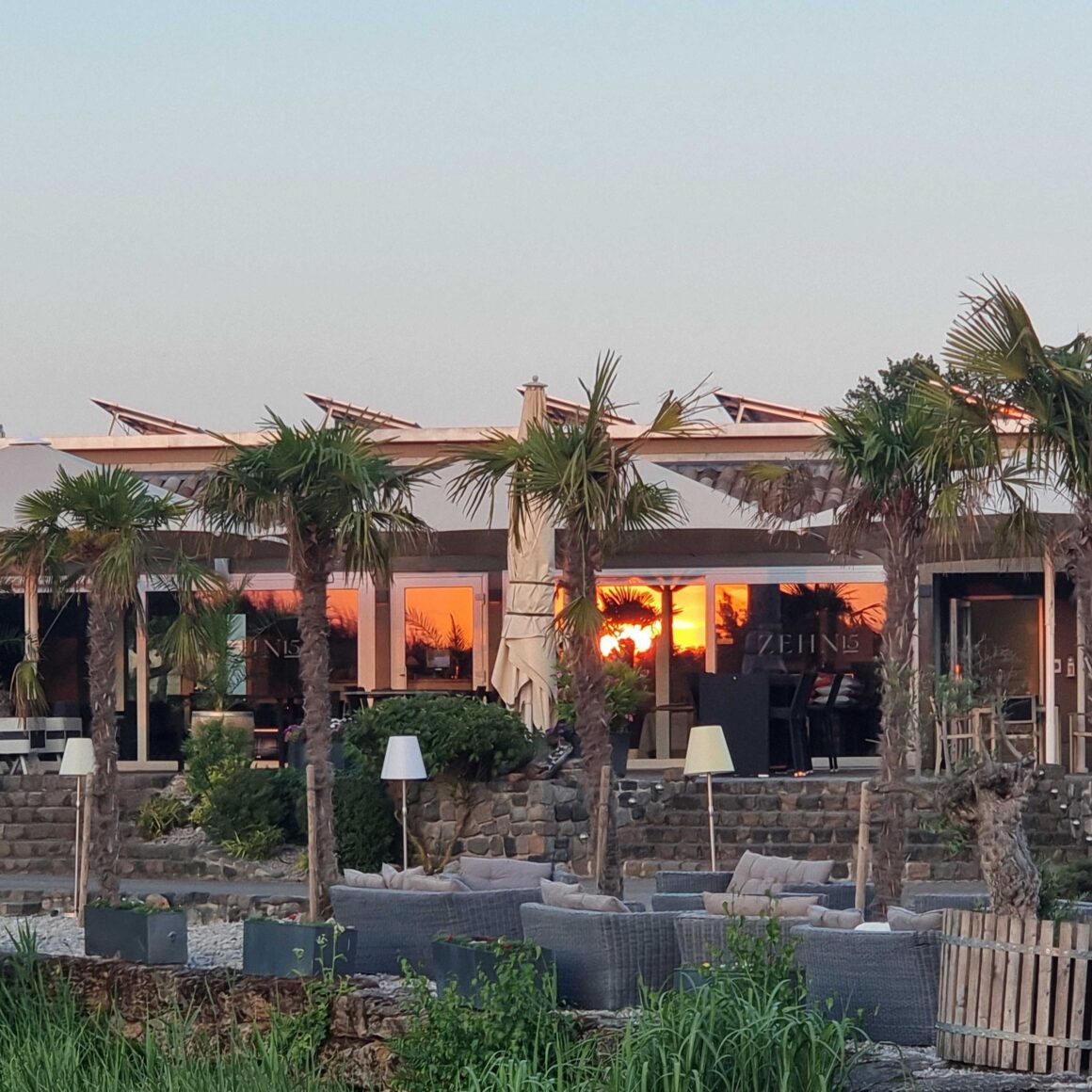 Außenbereich vom Golf Club Machern mit Sitzgelegenheiten, großen Sonnenschirmen und großen Palmen